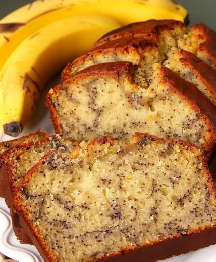 Sliced banana bread with a golden crust, speckled with banana pieces, served alongside ripe bananas.