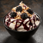 A luscious Blackberry Crumble dessert with creamy layers, fresh blackberries, granola, and a drizzle of blackberry sauce in a black bowl.