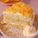 A slice of Orange Creamsicle Cake with layers of fluffy vanilla-orange cake and creamy frosting, garnished with orange zest.