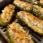 Crispy and cheesy air fryer stuffed pickles topped with melted cheese and breadcrumbs in a black air fryer tray.