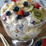 A creamy Cheesecake Fruit Salad in a glass bowl, loaded with fresh strawberries, blueberries, kiwi, bananas, and grapes, coated in a rich cheesecake dressing.