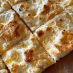 Close-up of freshly baked cottage cheese flatbread, cut into square pieces with a golden-brown, crispy crust and melted cheese.