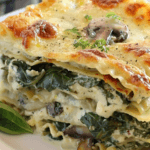 A close-up of creamy spinach and mushroom lasagna with layers of melted cheese, fresh spinach, and tender mushrooms.