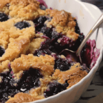 A freshly baked Delicious Blueberry Dump Cake in a white dish, featuring a golden crumble topping and a bubbling, juicy blueberry filling.