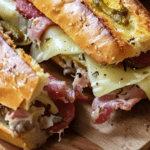 A close-up of a Giant Muffaletta Italian Sandwich with layers of meats, cheese, and olive spread on a sesame-crusted baguette.