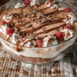 A rich and creamy chocolate cheesecake trifle layered with whipped cream, chocolate, and raspberries, topped with chocolate shavings and drizzled with chocolate sauce.