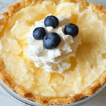 A creamy Lemon Impossible Pie with a golden crust, topped with whipped cream and fresh blueberries.