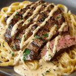 A plate of Cajun-seasoned steak, sliced and drizzled with creamy Alfredo sauce, served over fettuccine pasta and garnished with fresh parsley.