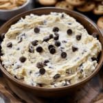 A luscious, creamy cookie dough dip loaded with chocolate chips in a rich brown bowl, surrounded by cookies and almonds.