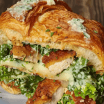 Flaky croissant sandwich filled with crispy chicken, melted cheese, fresh greens, and drizzled with a creamy herb sauce.