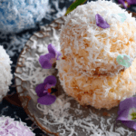 Close-up of Easter Bunny Coconut Tails, soft coconut-covered treats stacked on a rustic plate, garnished with edible flowers and shredded coconut