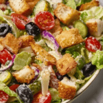 A bowl of Lovely Olive Garden Copycat Salad with crisp lettuce, cherry tomatoes, cucumbers, black and green olives, red onions, crunchy croutons, and creamy Italian dressing.