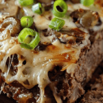 A close-up of Philly Cheesesteak Meatloaf topped with melted cheese, sautéed mushrooms, and green onions, showcasing its juicy and cheesy texture.