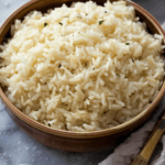 A warm bowl of fluffy souper rice, lightly garnished with fresh herbs, served in a rustic brown dish on a marble surface.