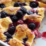 A freshly baked berry yogurt bake with a golden, crispy crust, bursting with juicy blackberries and raspberries in a white baking dish.