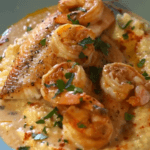 A plate of red snapper and shrimp over creamy grits, topped with Cajun cream sauce, garnished with fresh parsley and spices.