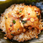 Tender roasted chicken glazed with a flavorful sauce, served over fragrant sticky rice, garnished with peanuts, chili, and green onions.