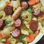 A hearty bowl of sausage and cabbage stew with sliced sausage, tender cabbage, carrots, and fresh herbs in a savory broth.