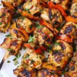 Juicy, grilled chicken kebabs with bell peppers, garnished with fresh herbs, served on a white plate.