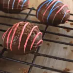 Chocolate-covered peanut butter Easter eggs decorated with colorful drizzle and cookie crumbs, cooling on a wire rack.