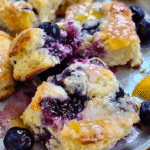 Fluffy lemon blueberry biscuits topped with melted butter and glaze, surrounded by fresh blueberries and lemon slices.
