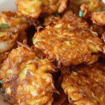 Close-up of crispy golden Amish onion fritters in a white bowl, garnished with chopped green onions.