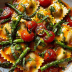 A rustic plate of ravioli topped with blistered cherry tomatoes, sautéed asparagus, fresh herbs, and garlic in a light tomato-based sauce.