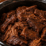 Close-up of homemade Crock Pot Texas-style boneless beef ribs inside a black slow cooker, coated in rich smoky barbecue sauce with visible cracked pepper seasoning and caramelized bark.
